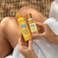 Two bottles of dip body oil held by a person with a textured background